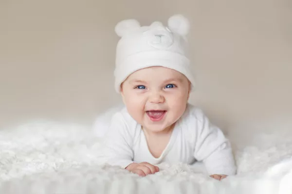 A Portrait Of A Cute Newborn Baby In A White Like A Bear Cub Hat Lying On Its Stomach And Laughing